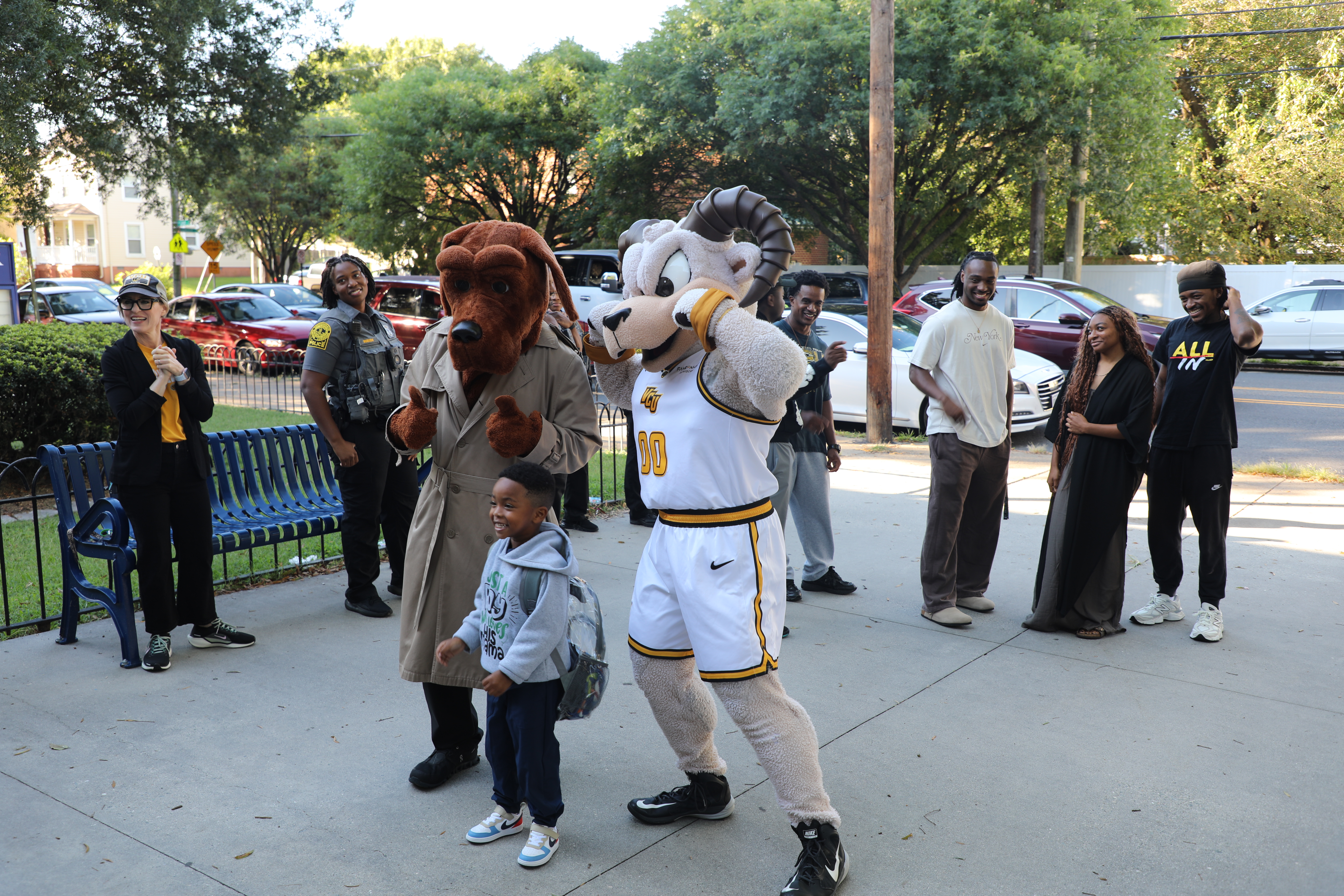 VCU’s Rodney the Ram and McGruff the Crime Dog pose with a young child while adults nearby smile and watch outdoors.