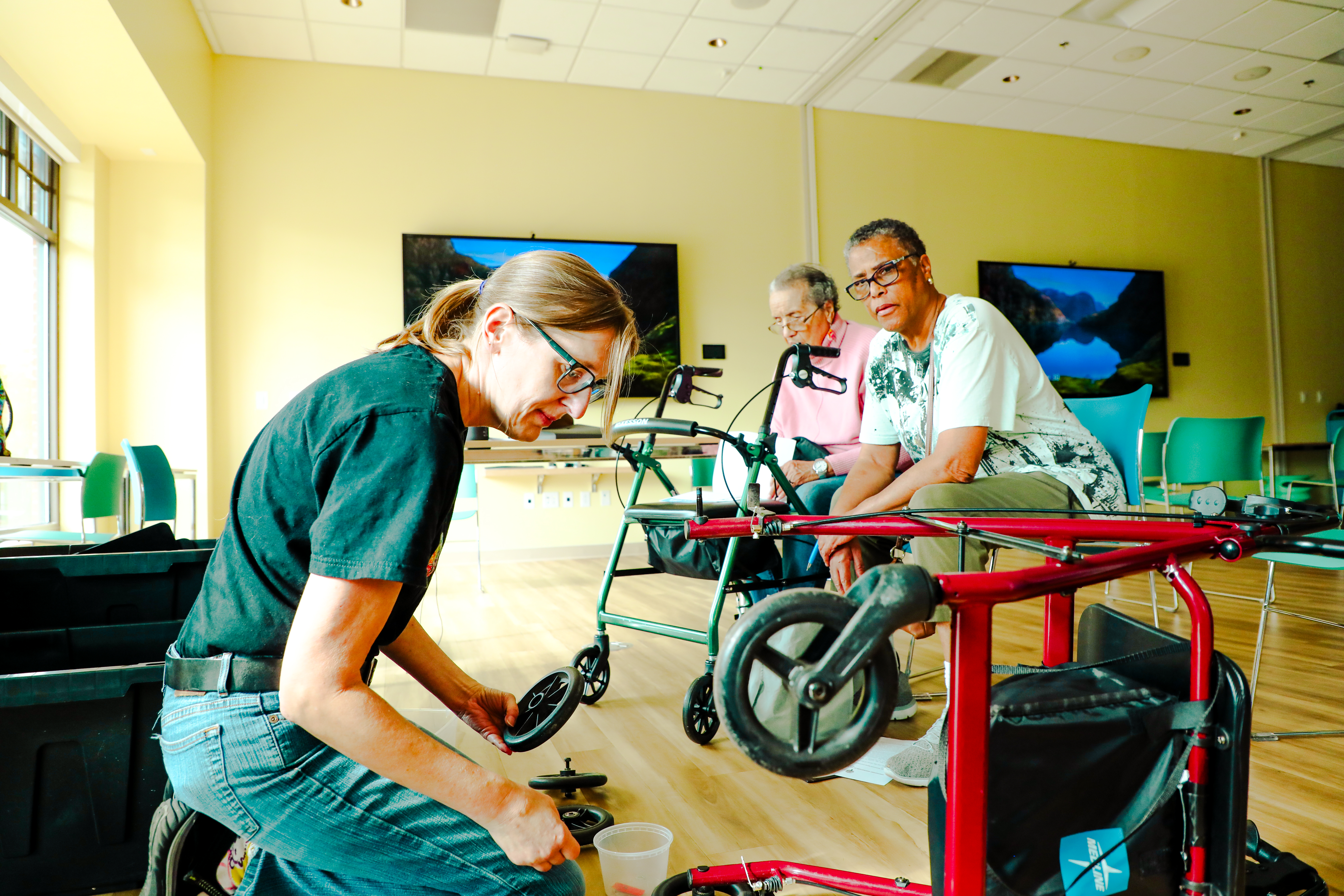 A woman helping another women tighten wheels on rollator