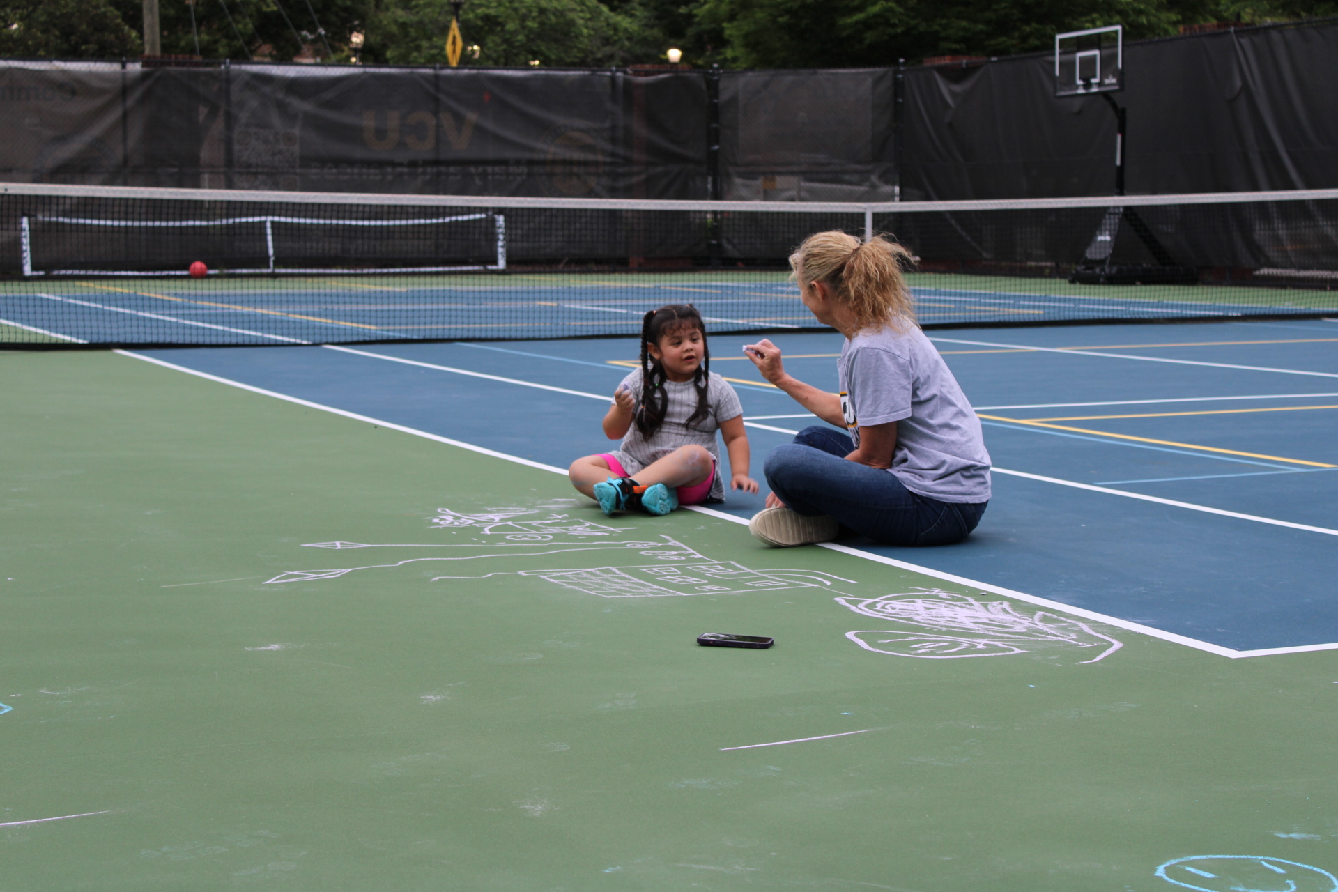 woman playing chalk with young girl on tennis court