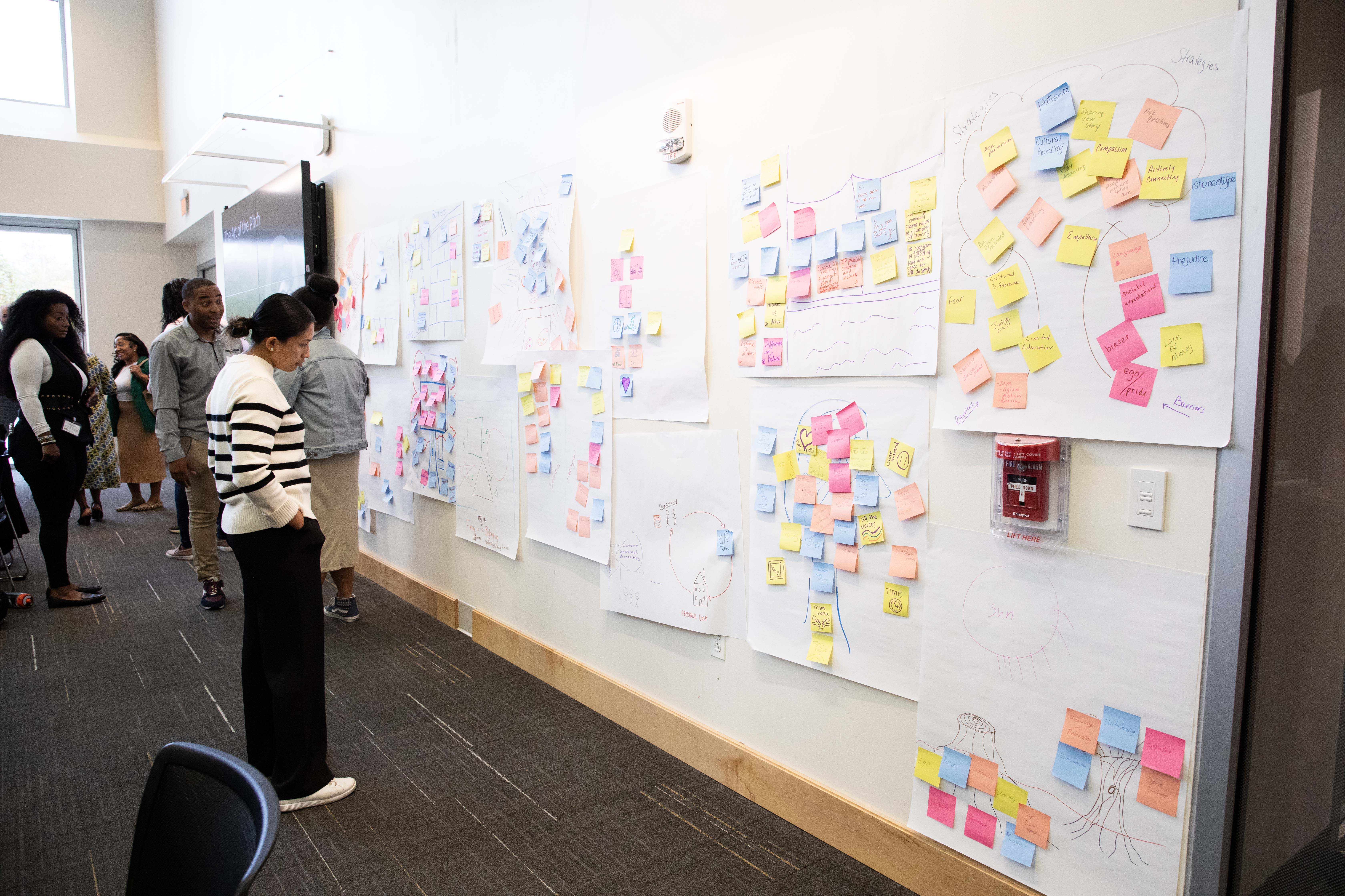 A woman looking at a wall of giant sticky note full of drawings from group activities