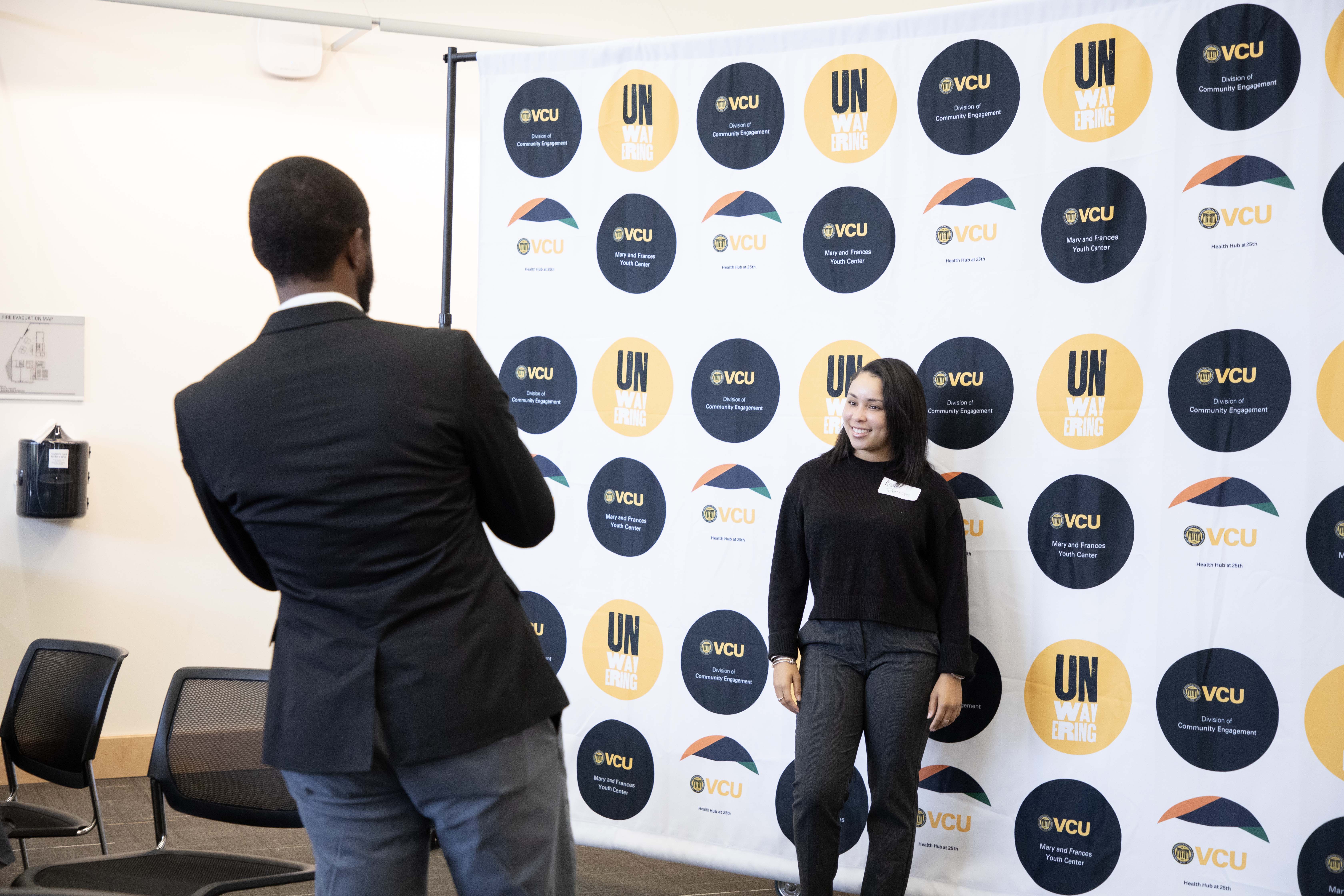 A man taking a picture of a women in front of a step and repeat sign