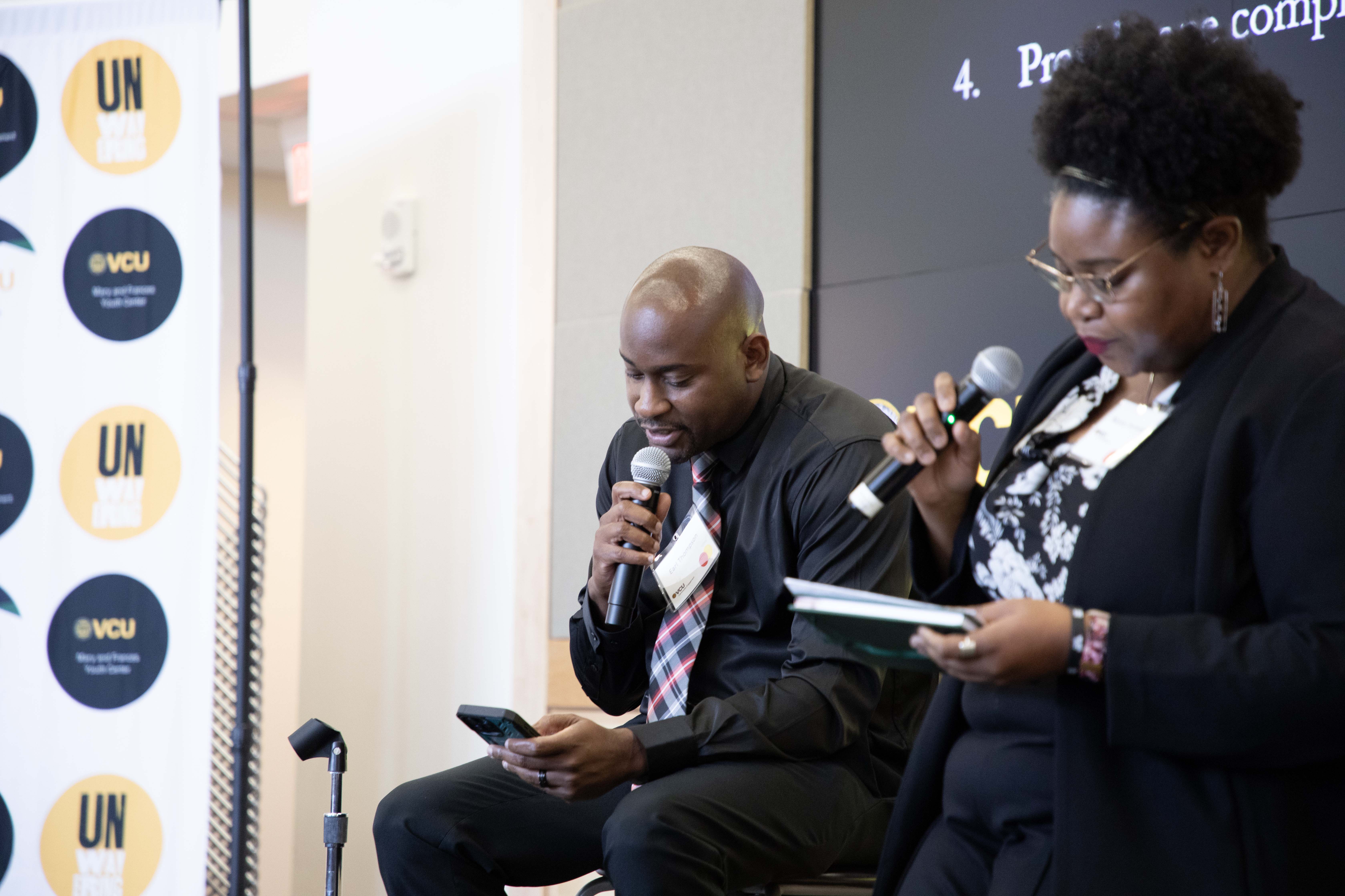 A man speaking into a microphone and reading off his cell phone